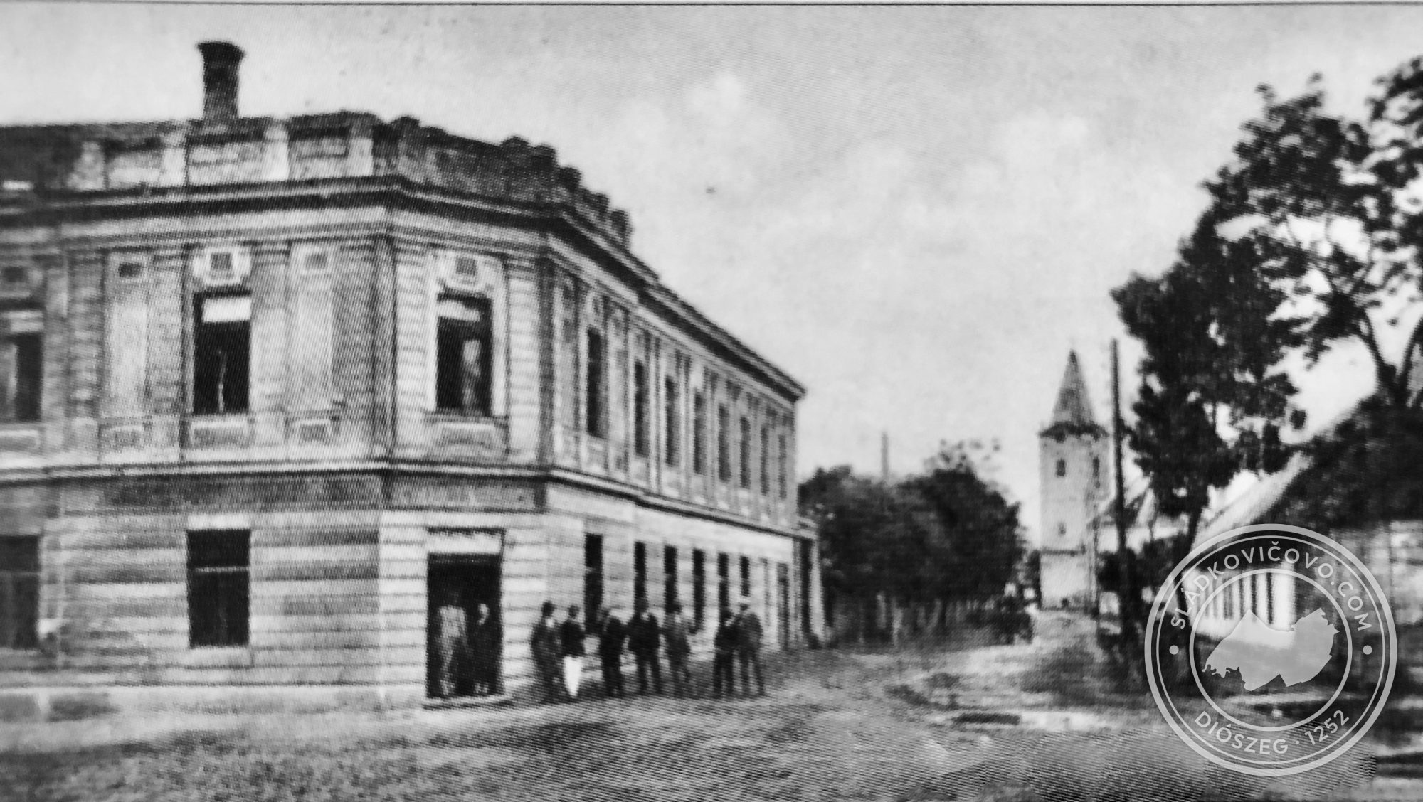 A Cukorgyári utca valamikor a 20. század harmincas éveiben. Balra a Wollner-ház, a háttérben a templom. A fényképész háta mögött (a képen kívül) a kaszinó épülete áll.