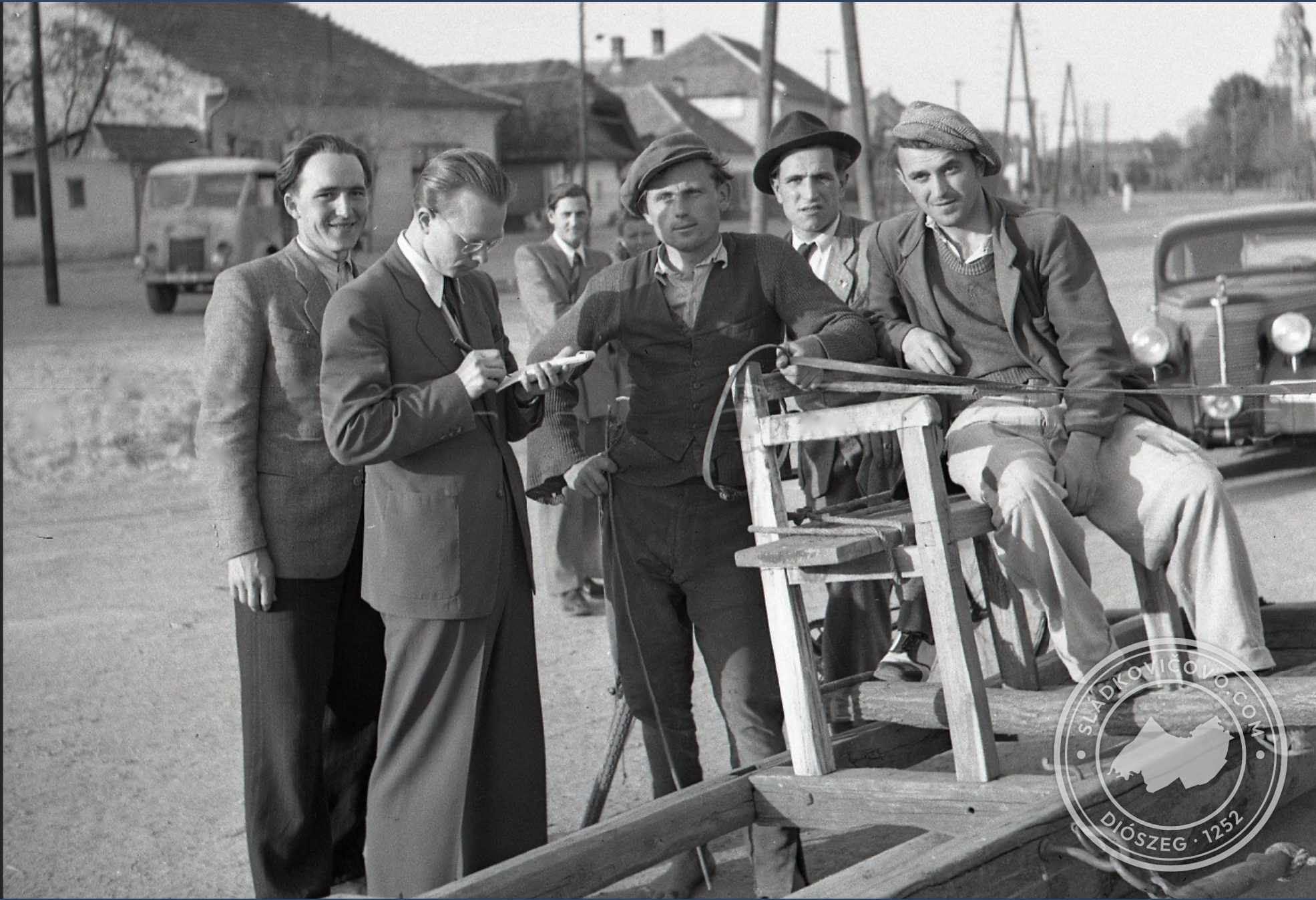 Fotografia vyhotovená v roku 1947 na námestí. V slnečnom jarnom počasí sa vykonávala úprava plochy námestia valcovaním s párom koní. Na pozadí ešte pôvodná zástavba.